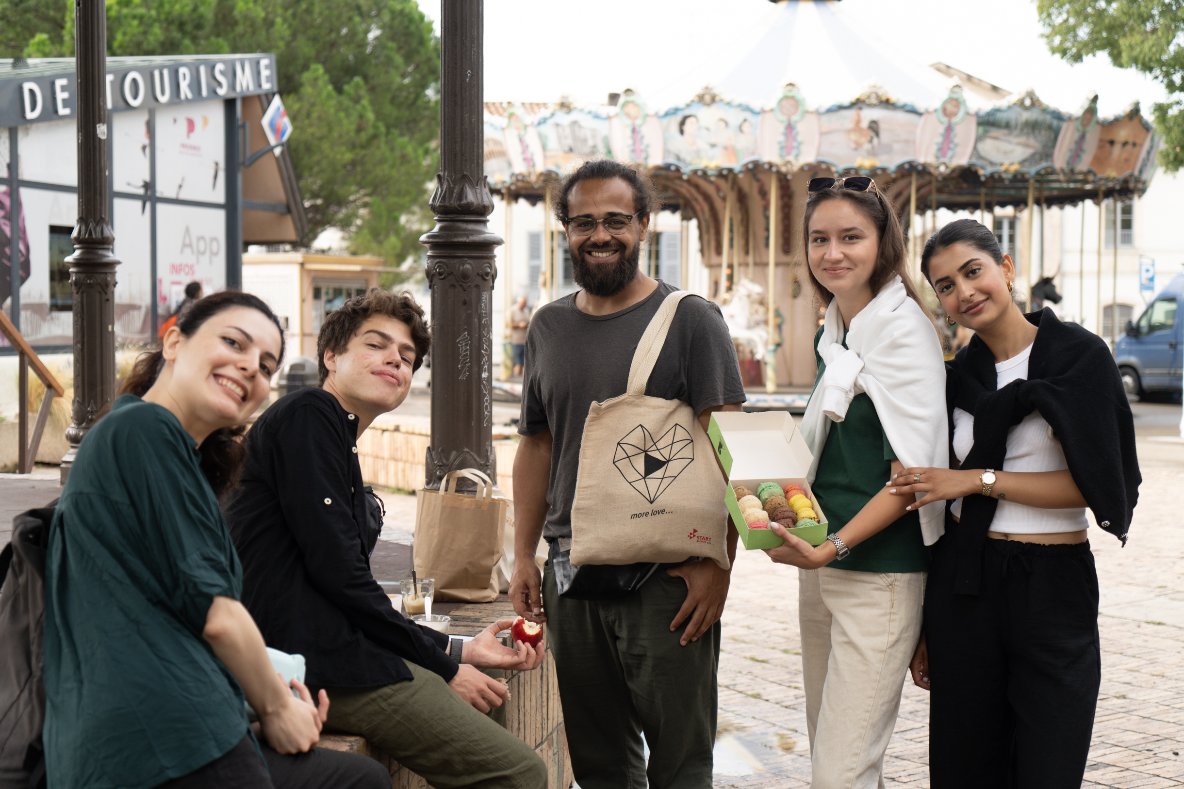 START-Alumni e.V in Arles beim Fotofestival. Das Foto zeigt fünf junge Personen auf dem Wochenmarkt in Ales. Im Hintergrund ist ein historisches Karusell zu sehen.